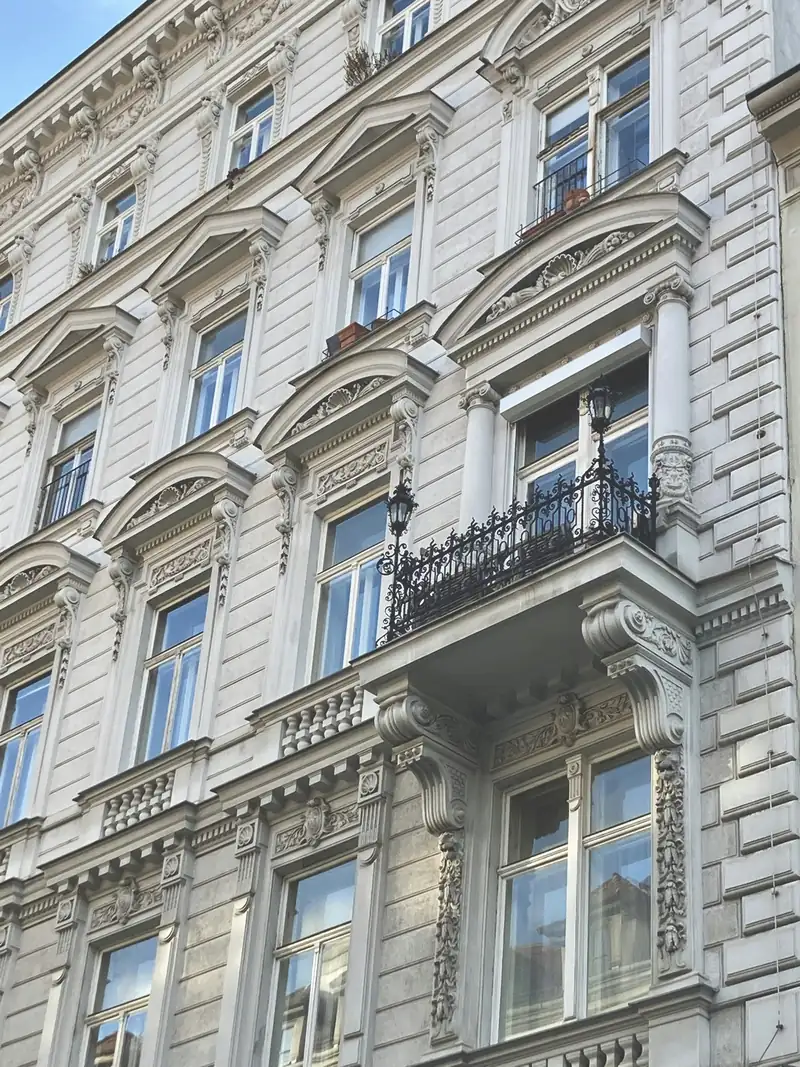 Frisch sanierte weiße Wiener Gründerzeitfassade mit Stuck, Fensterverdachungen und schmiedeeisernem Balkon