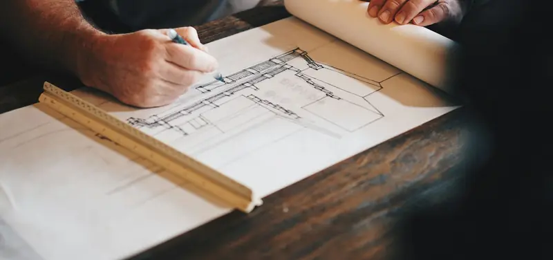 Baumeister zeichnet einen Bauplan mit Lineal am Schreibtisch